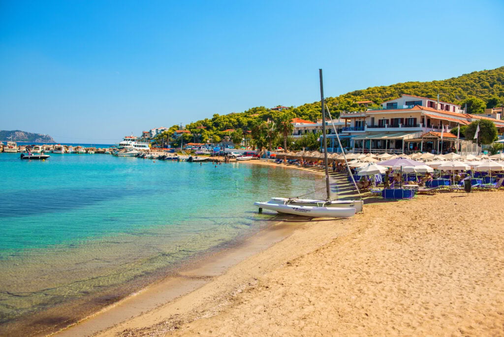 En mjuk sandstrand med små båtar och turkost vatten.