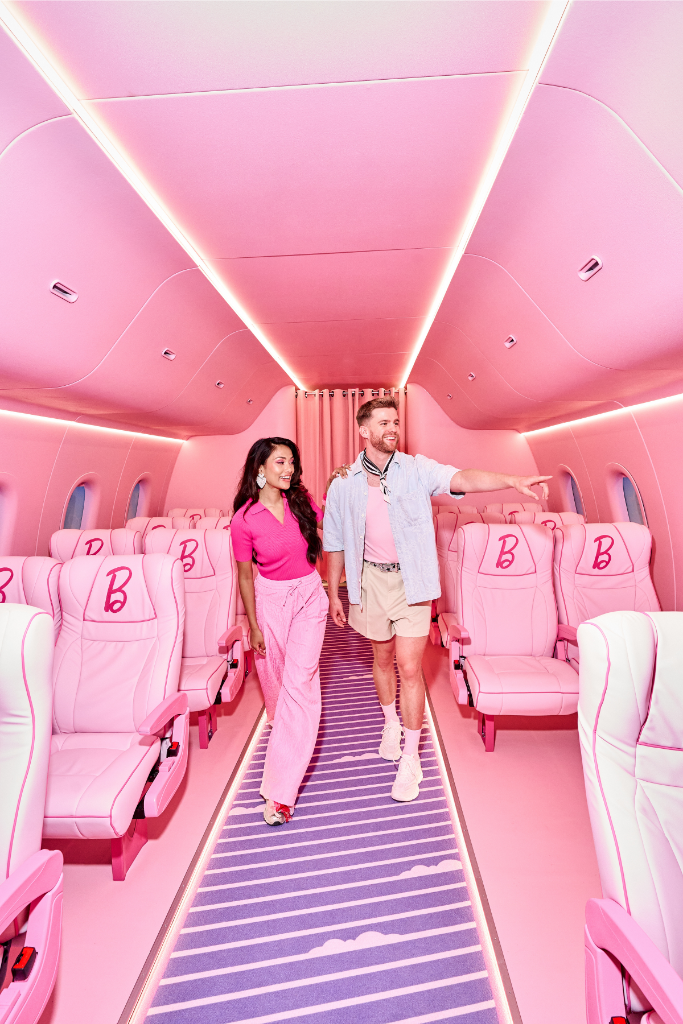 En rosa flygkabin med rosa stolar och lila matta. Två personer går genom gången. 