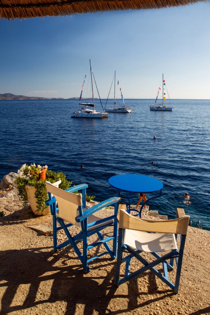 table and 2 chairs in cafe on amazing Greek island Hydra and yachtssyaing at distance. View from Hydra greek island