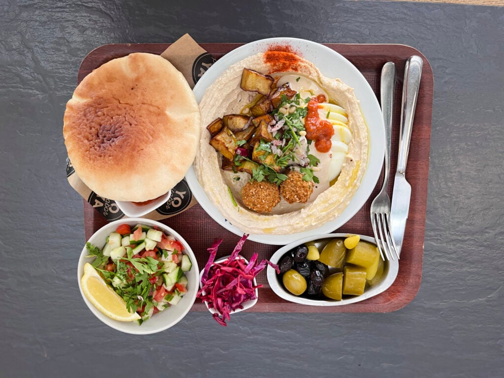 En bricka med flera tallrikar med falafel, humus, bröd och picklade och färska grönsaker.