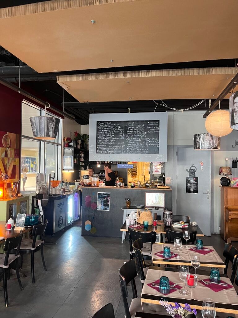 En liten lokal med dukade bord och stolar och en kafédisk. 