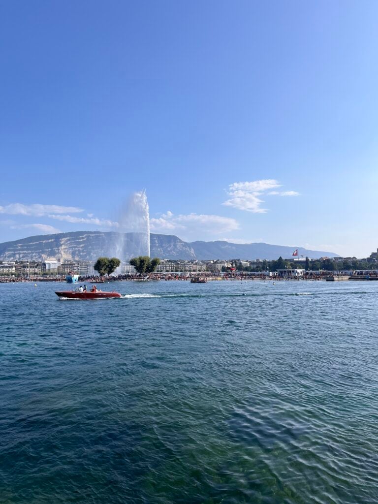 En blå sjö med en båt som cruisar. Staden syns bakom, med ett bergslandskap i horisonten. 