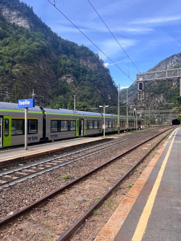 Ett tågspår mellan lummiga berg, tåg står vid perrongen. 