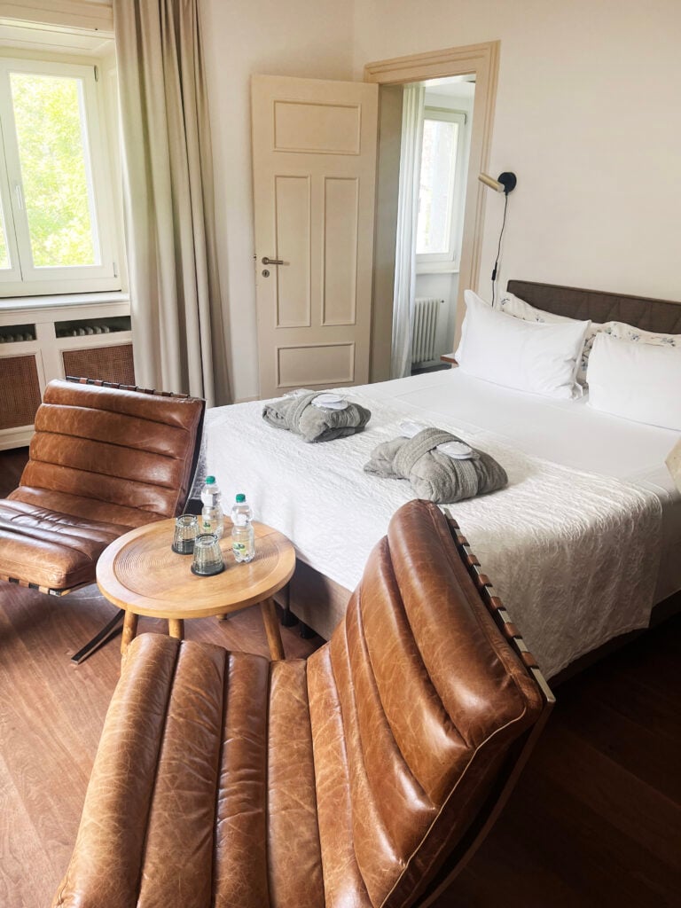 Läderfåtöljer bredvid en ljust bäddad säng i ett hotellrum. 