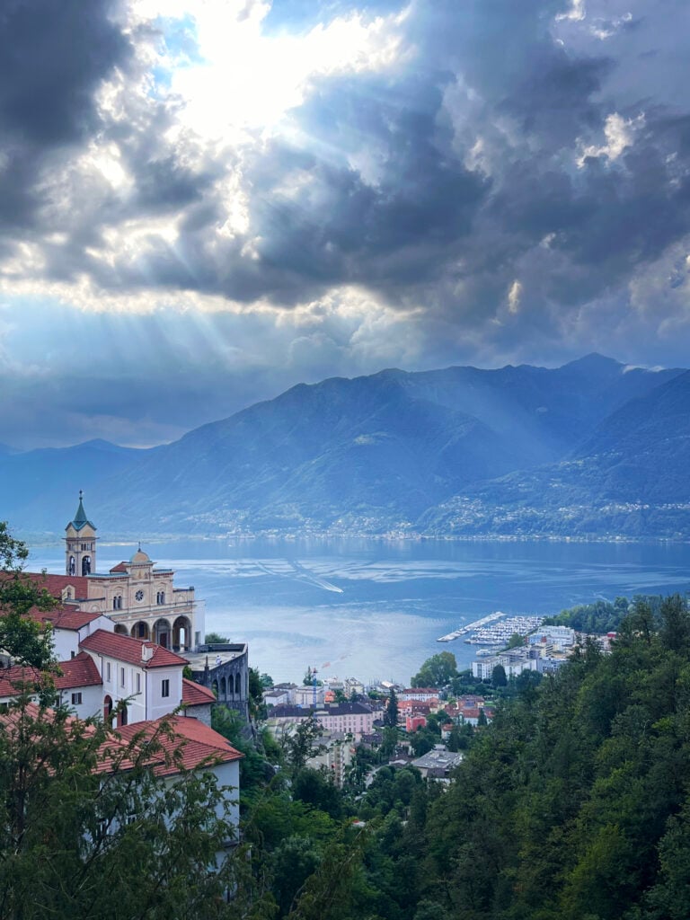 En mörkblå, disig sjö fotas från hög höjd. Klassisk arkitektur syns på bergssidorna, på andra sidan sjön är det dramatiska berg. 