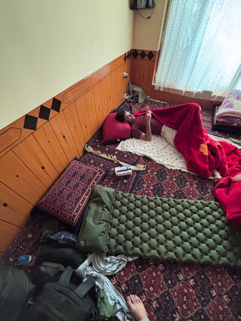 Ett grönt liggunderlag på  persiska mattor, en man i lila t-shirt ligger bredvid under en röd filt. 