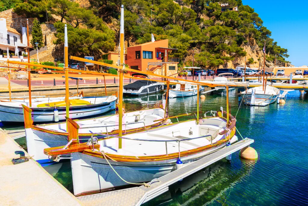 Traditionell liten vit fiskebåt ligger vid en brytta med en lummigt grön kust bakom.