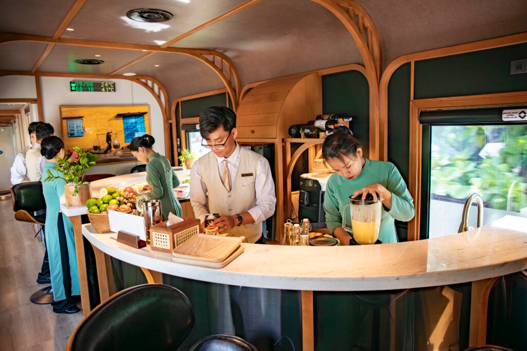 Tre anställda i eleganta gröna och vita kläder står bakom en lyxig bardisk. 