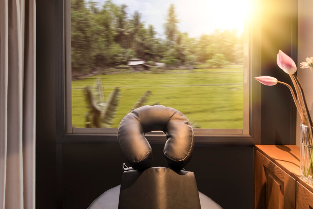 En massagestol syns framför ett tågfönster med grönt landskap. 