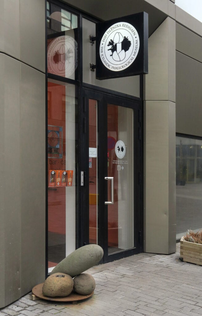 En stilren museientré, med en skulptur av tre stenar, organiserade så att de liknar ett manligt könsorgan.