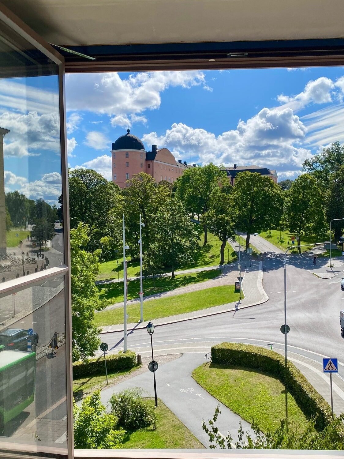 Ett öppet fönster visar ett grönskande uppsala, bilvägar och Uppsala slott som sticker upp. 