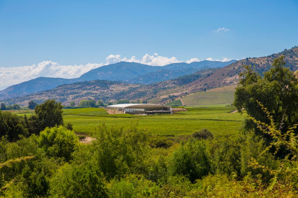 En stor byggnad på ett grönt fält framför enorma bergstoppar.