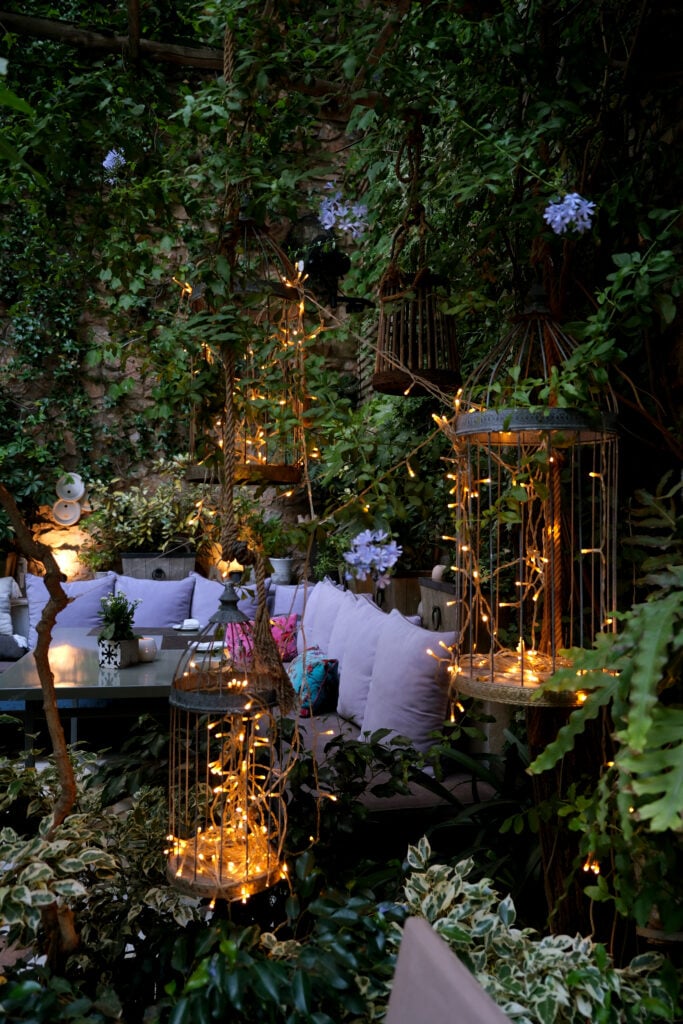 En soffa med kuddar är omgärdad av ljusslingor och prunkande grönska på väggarna.