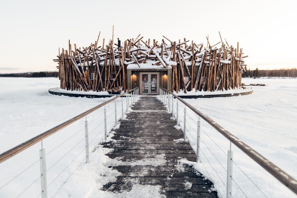 En smal brygga med räcken leder fram till en fågelboliknande byggnad, allt är täckt av snö och is.