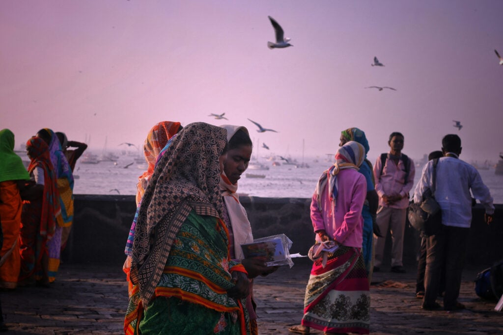 Flera kvinnor klädda i traditionella indiska tyger, på en strand med rosa kvällsljus.