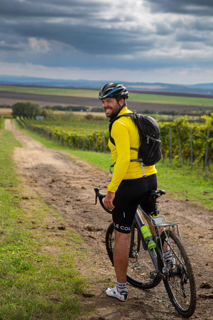 Man i gul jacka på cykel mellan vinbuskar.