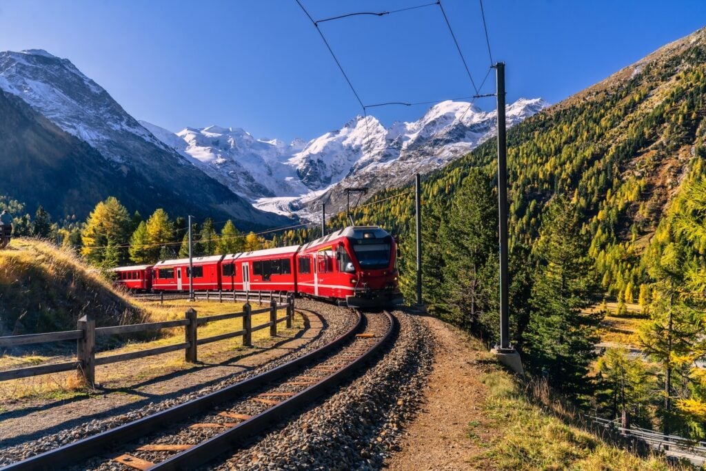 Rörr schweiziskt tåg på väg upp i Alperna med glaciär i bakgrunden.