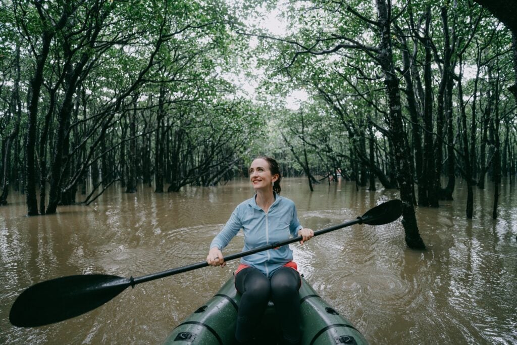 Kvinna i kanopt som paddlar i flod med träd.