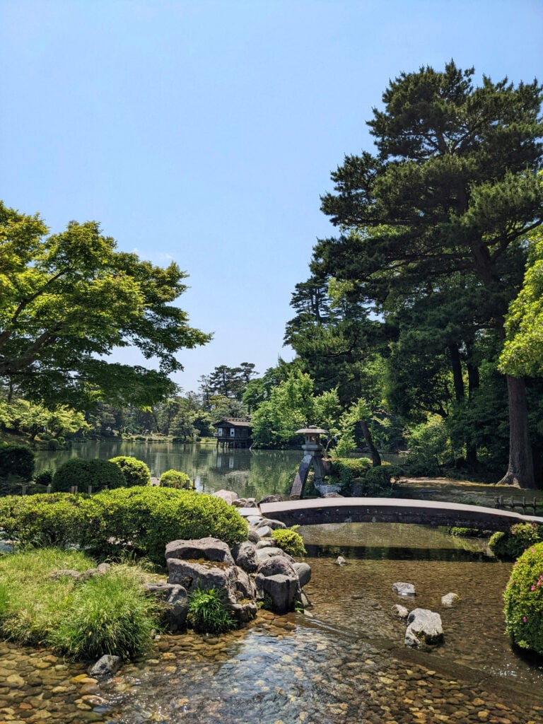 En lummig japansk park med en damm och en liten gångbro i sten.