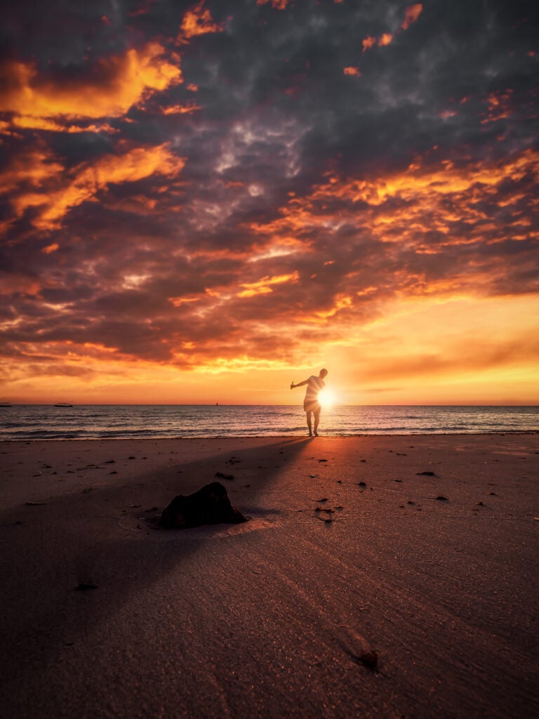En person står på en strand som badar i solnedgångsljus.