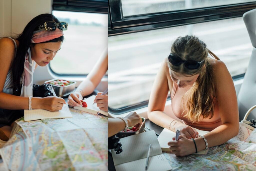 Två tjejer som sitter på tåg och planerar sin tågluff med hjälp av papperskartor.