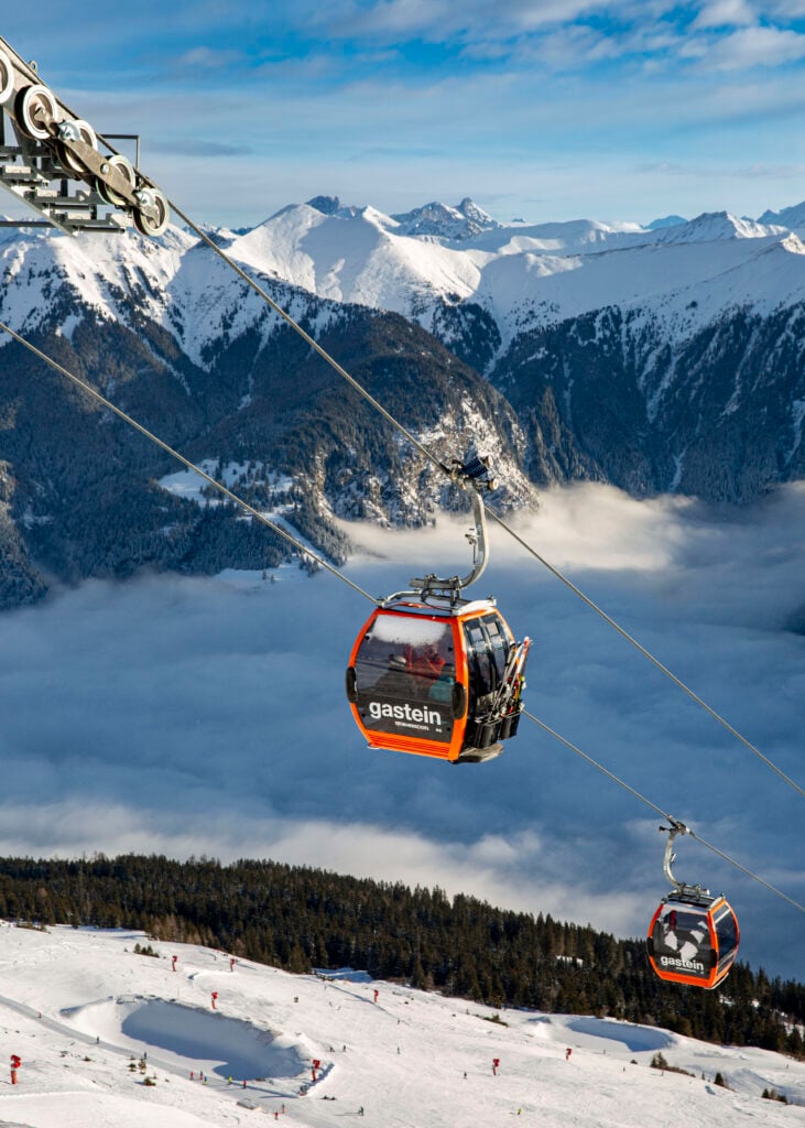 Kabinbanor i orange går genom bergen. Skidbacke under.  