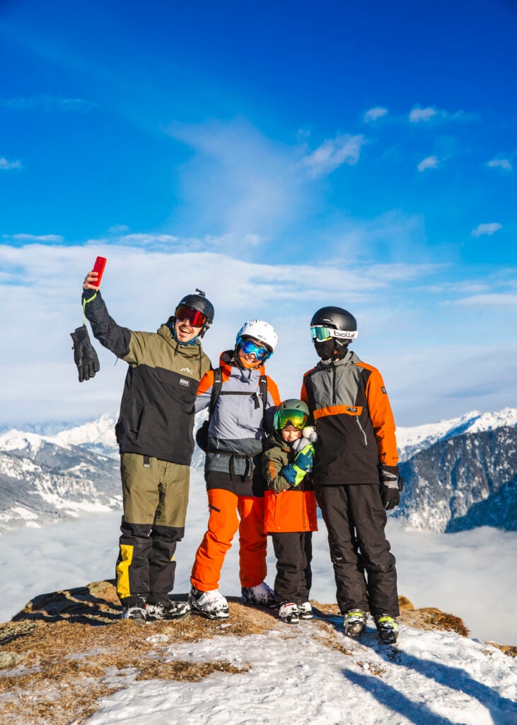 Tre vuxna och ett barn poserar framför kameran på en bergstopp, i skidkläder. 