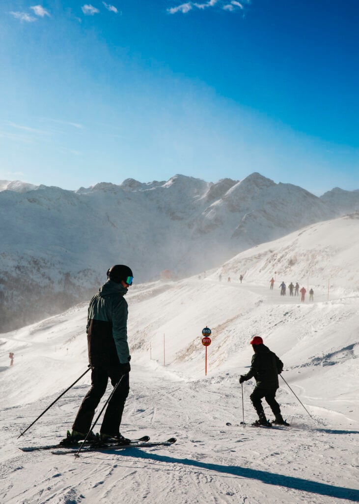 Två personer åker skidor nedför en pist. 