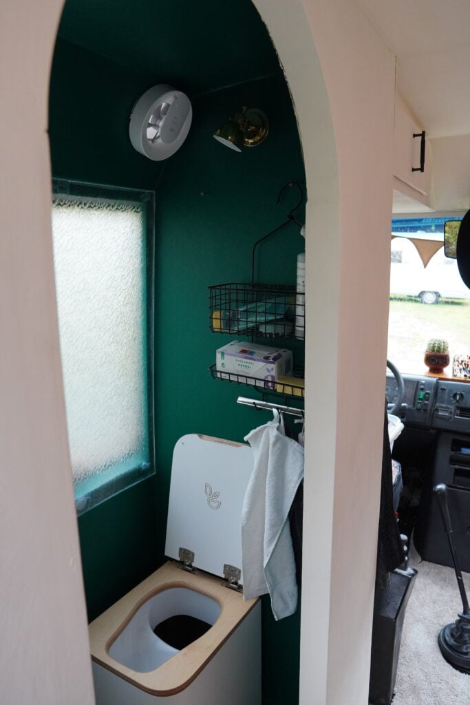 Ett grönt badrum med en välvd dörr och en toalett. 