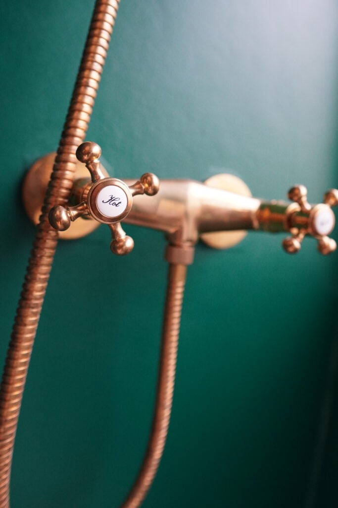 Guldfärgade kranar, slang och blandare syns mot en grön vägg. 