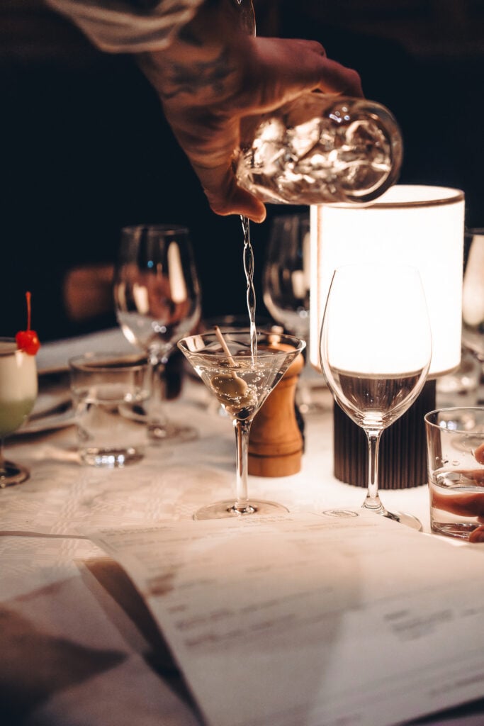 En hand häller upp drinkar på ett dukat bord med martiniglas.