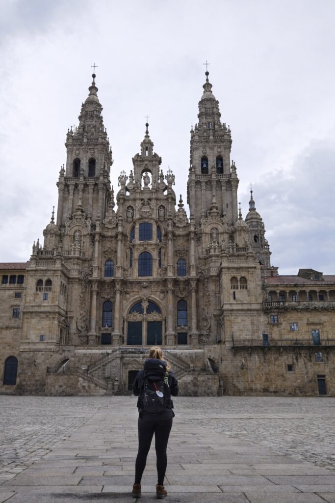En kvinna står framför en gotisk katedral med tinnar och torn.