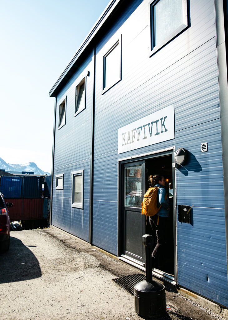 En person med gul ryggsäck går in i ett blått plåthus med skylten "Kaffivik".