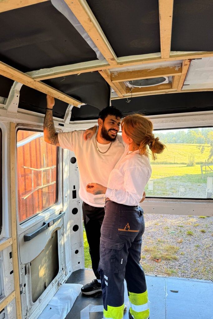 Två personer kramas i byggkläder i en buss som är under konstruktion.