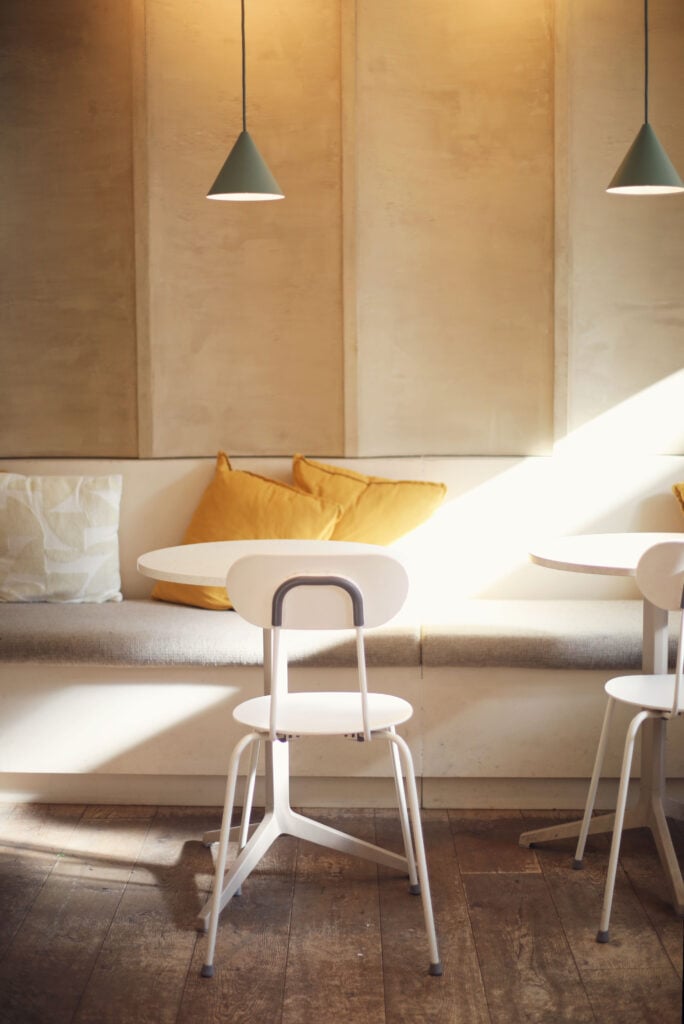 Beigea väggar, gråa bänkar, gula soffkuddar. Solen skiner in i rummet. 