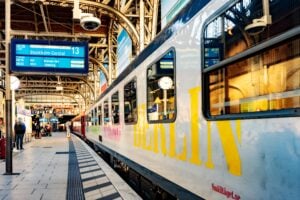 Ett vitt tåg med texten BERLIN målat i gult står på en tågperrong. Avgångsskylten markerar att tåget går mot "Stockholms Central"