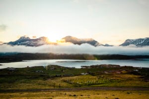 Utsikt över en liten by framför ett kallt hav med dramatiska berg bakom.