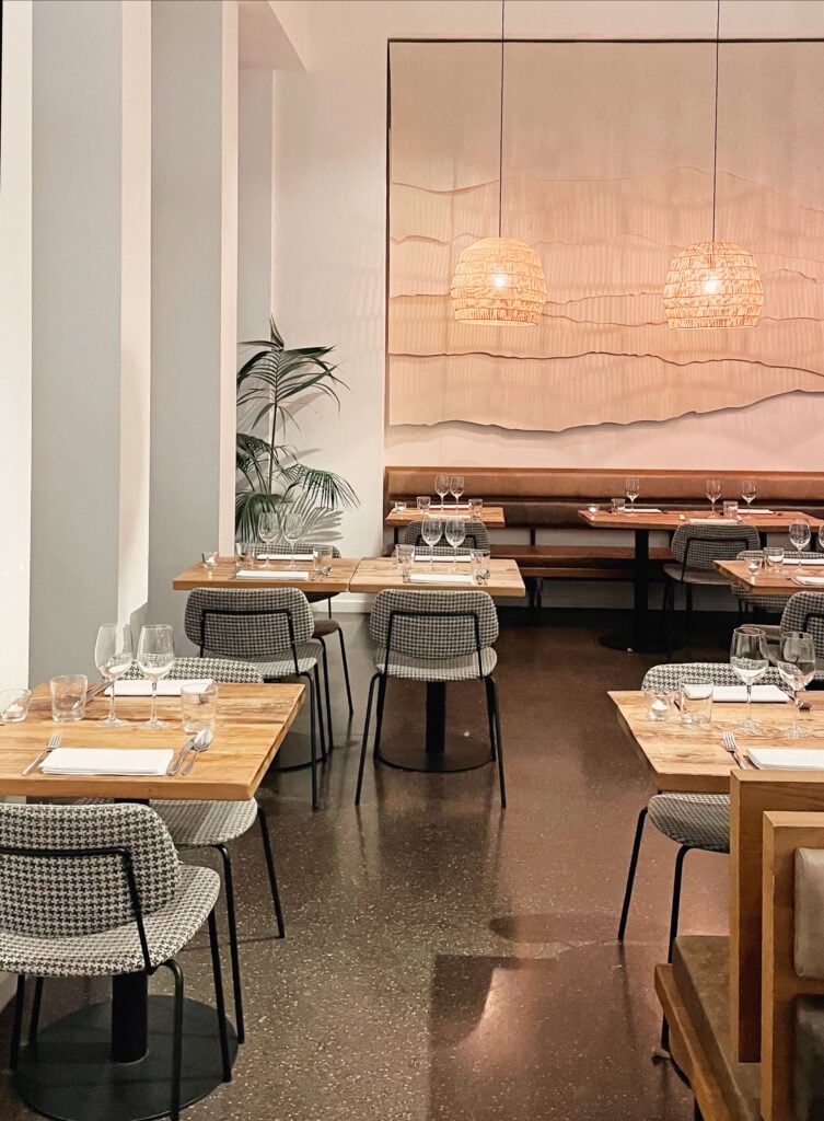 En ljus restaurang med små träbord och gråa stolar, mysig belysning. 