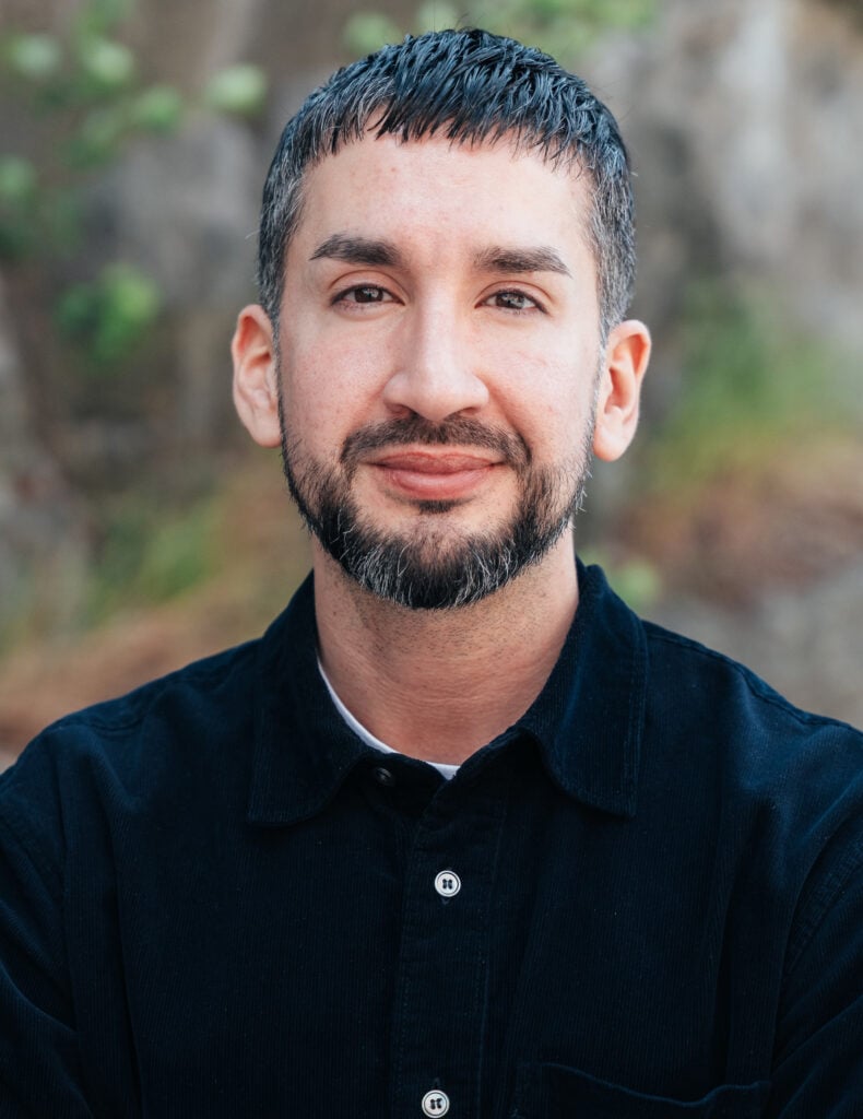 En man i kort hår och skägg ler mot kameran.