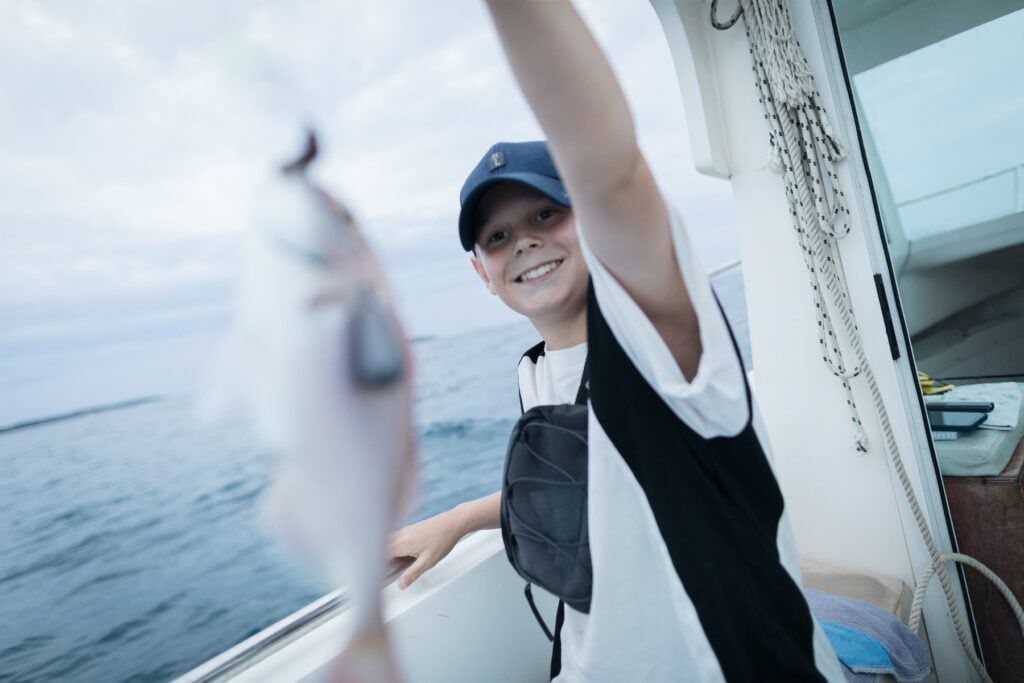 Pojke med fångade fisk på båt.