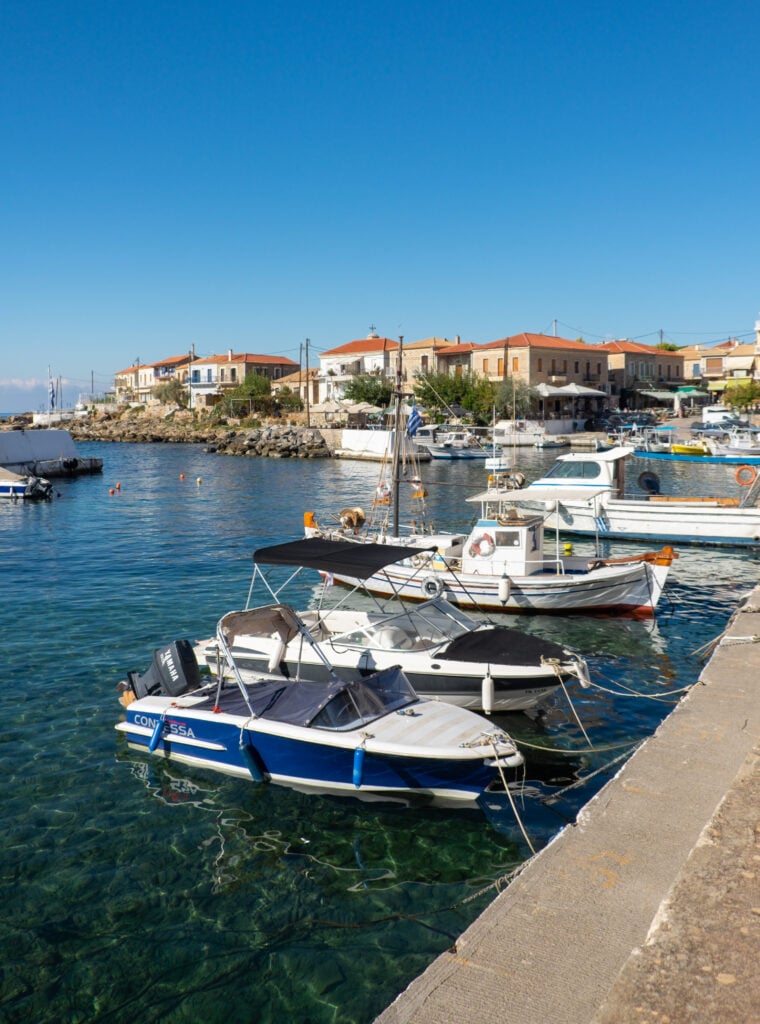 Emå båtar ligger förtöjda mot en betongkaj. Små hus i bakgrunden.