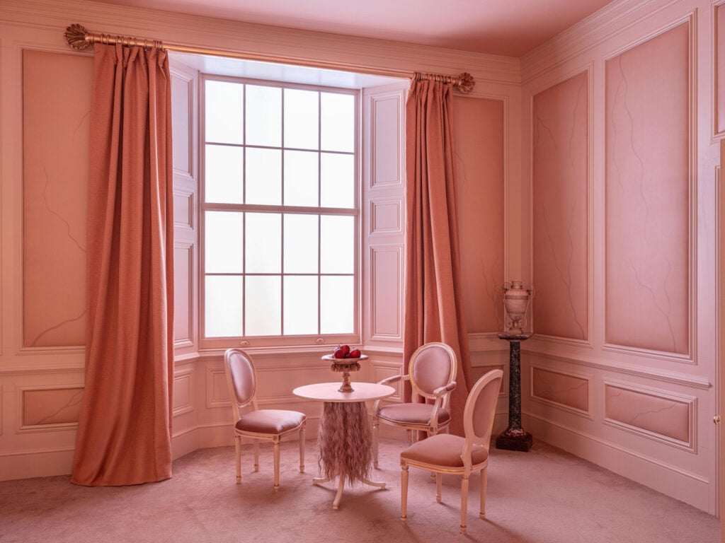 Rosa väggar, rosa bord och stolar, stort fönster. 