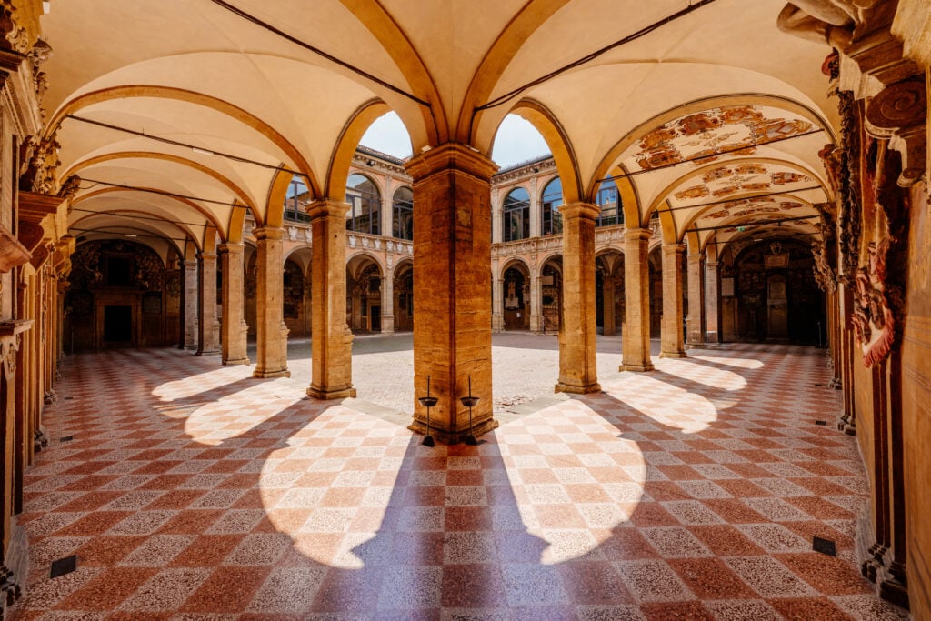 Rutigt golv, välvda arkader och bågar, ett torg med solsken.