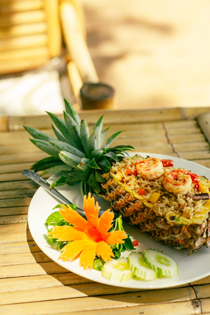 En ananas fylld med någon risrätt ligger på en tallrik med färska grönsaker.