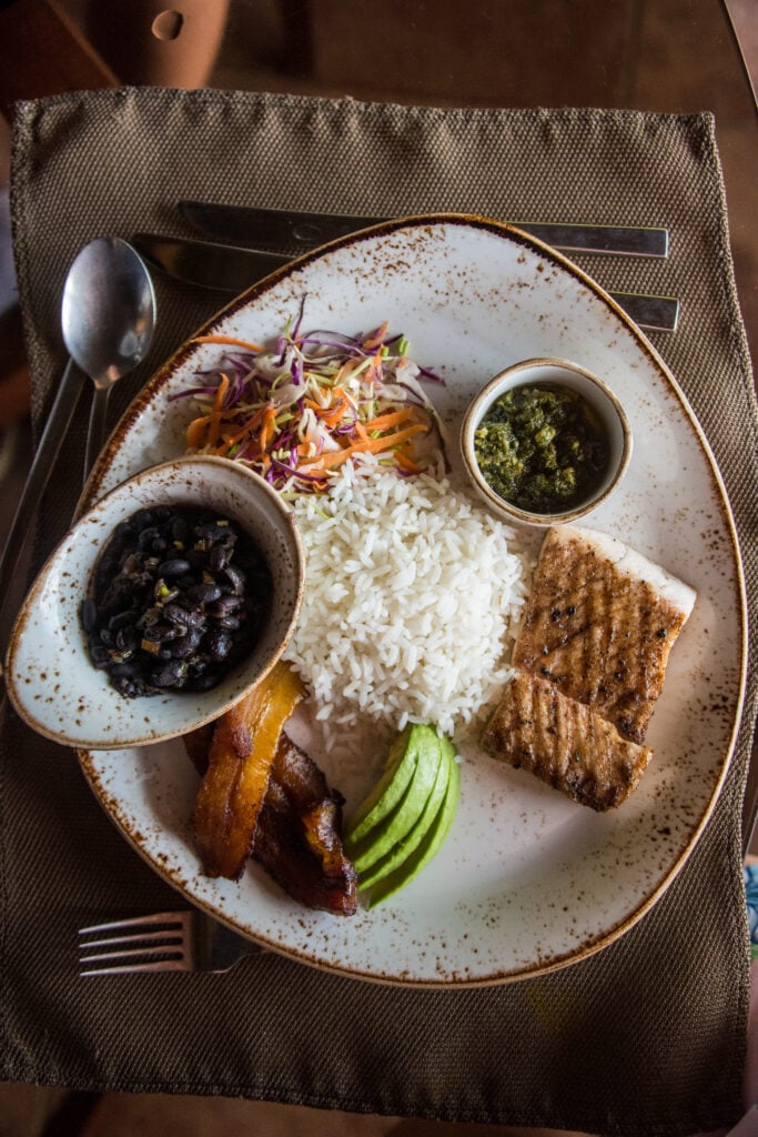 En tallrik med ris, grönsaker, skålar med bönröra, grillad fiskfilé. 