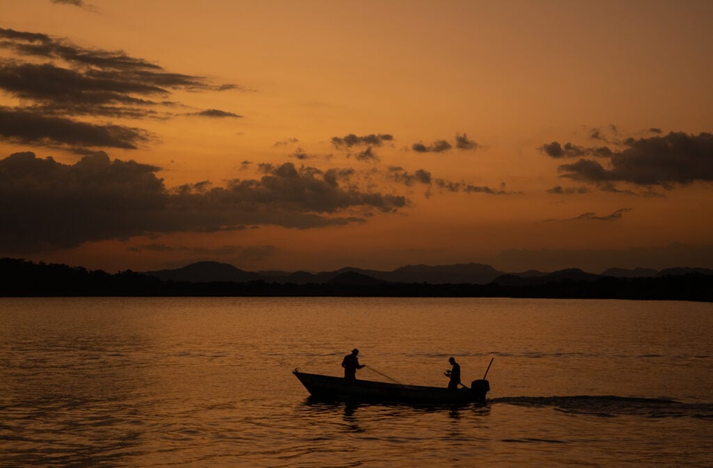 Två personer sitter i en liten fiskebåt i solnedgången. 