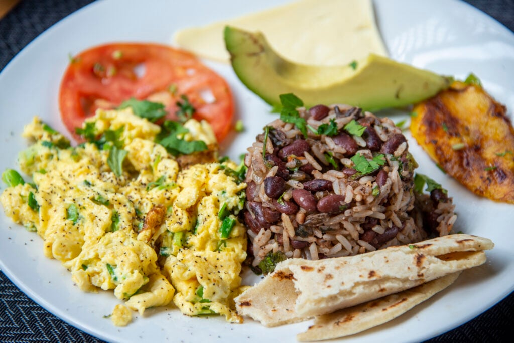 En tallrik med äggröra, tomat, avocado, ris- och bönröra och ett ihoprullat bröd. 