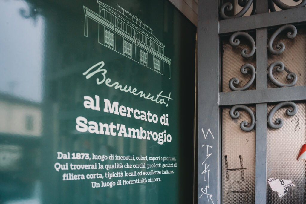 Green welcome sign at the entrance of the historic Mercato di Sant'Ambrogio, Florence, Italy, inviting people to discover local products