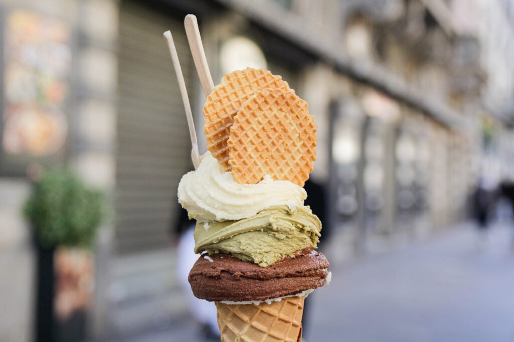 En glasstrut med choklad, pistage och vit glass, med runda kex på toppen.