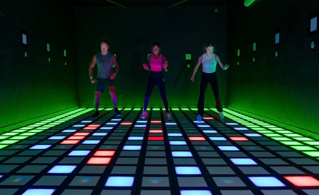Tre personer står på ett lysande golv med rutor och gröna lysande väggar.
